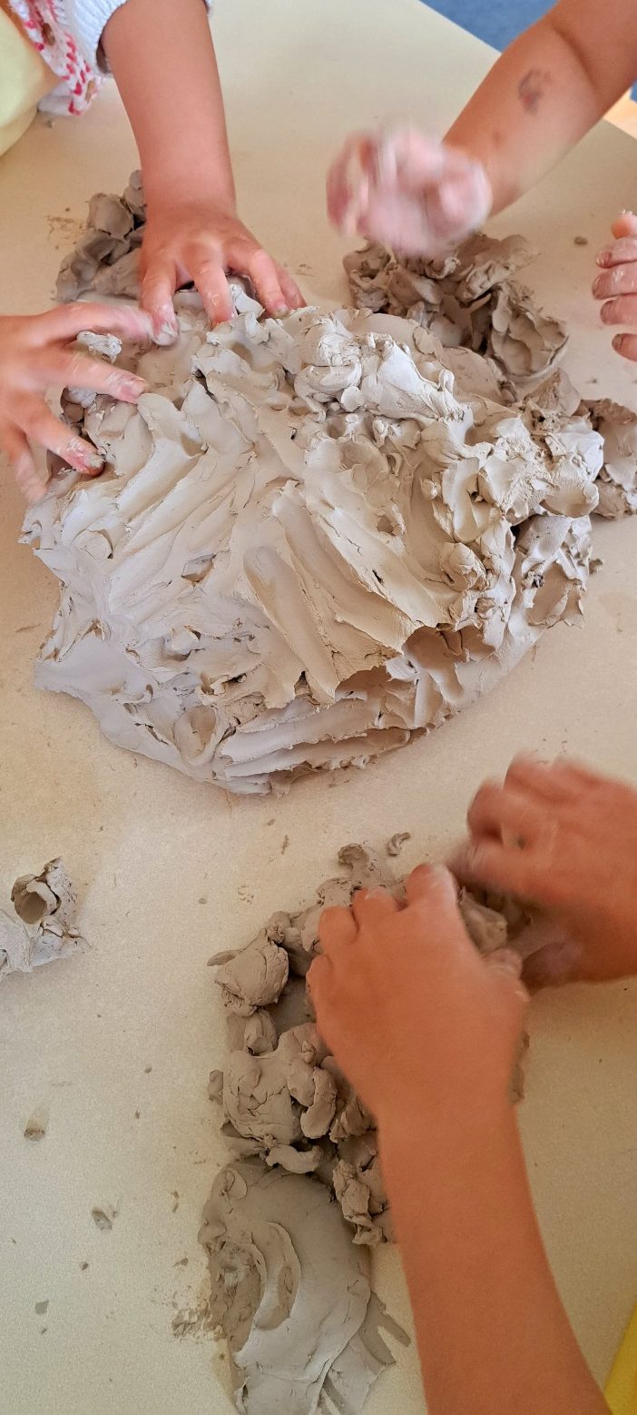 Kinder formen spielerisch mit grauem Knete an einem Tisch.