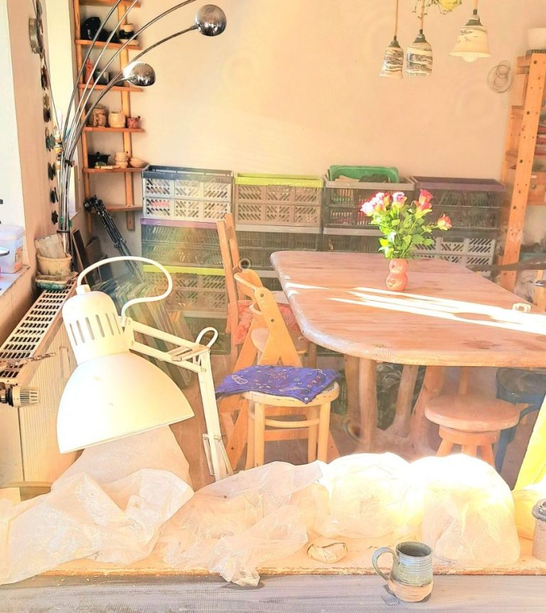 Arbeitsbereich mit Lampen, Tischen und Tontöpfen, umgeben von weißem Material.