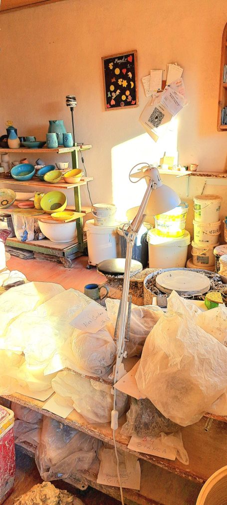 Helle Werkstatt mit Töpferutensilien, Regalen und einer Stehlampe im Vordergrund.