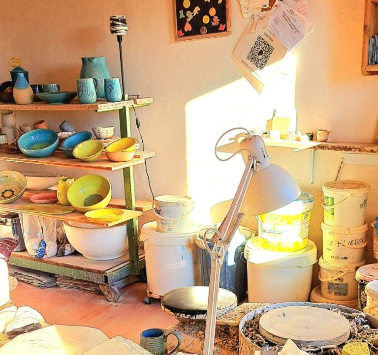 Helle Töpferei mit bunten Töpfen, Regalen und Werkstattutensilien.