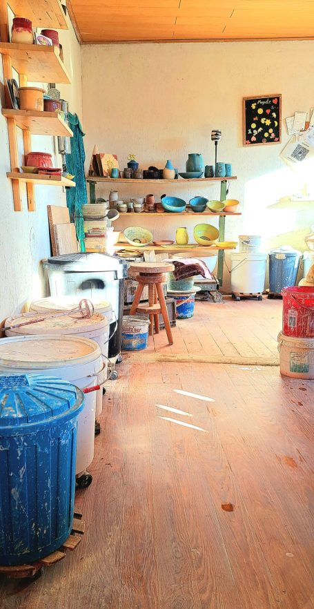 Blick auf einen Raum mit Regalen, Behältern und einer Holzbank im Vordergrund.