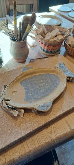 Holzteller mit einer Fischform, umgeben von Körben und Werkzeugen auf einem Tisch.