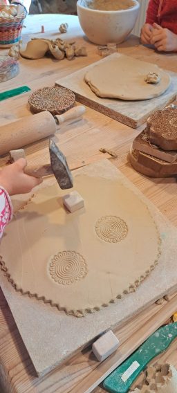 Ein Kind bearbeitet Ton auf einem Tisch mit Werkzeug und verschiedenen Tonstücken.