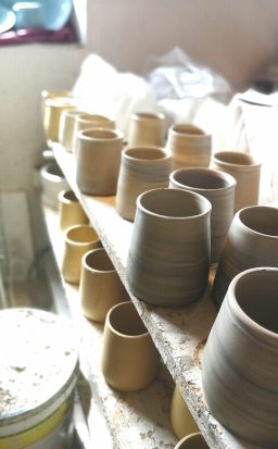 Reihe von ungebrannten Tontassen auf einem Regal in einer Werkstatt.