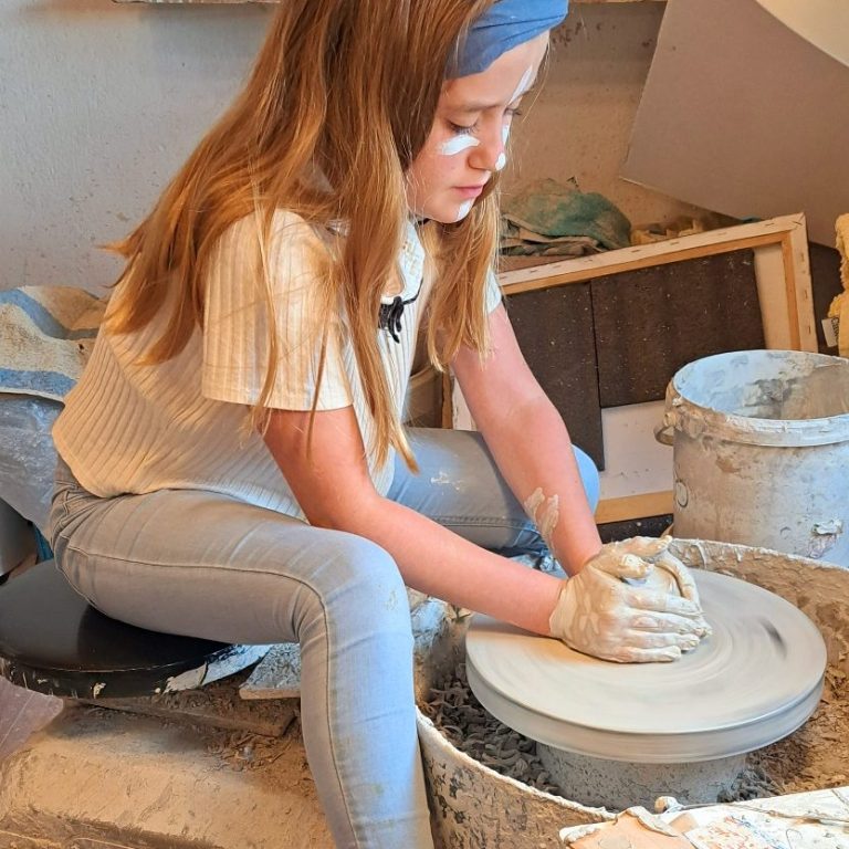 Ein Mädchen formt Töpferwaren auf einer Drehscheibe in einem Atelier.