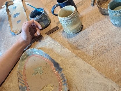 Hand auf einem Tisch mit verschiedenen Töpferwaren und Werkzeugen.