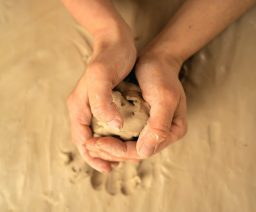 Hände formen einen Ball aus feuchtem Ton auf einem Tisch.