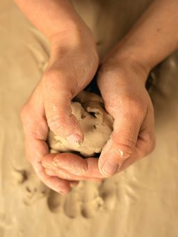 Hände formen einen kleinen Ball aus Ton auf einer neutralen Oberfläche.