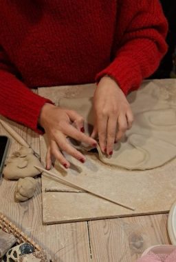 Hände formen Ton auf einem Tisch, umgeben von Kunstmaterialien.