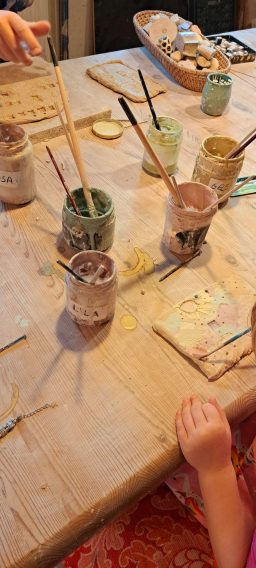 Farben und Pinsel auf einem Tisch, Hände eines Kindes sind sichtbar.