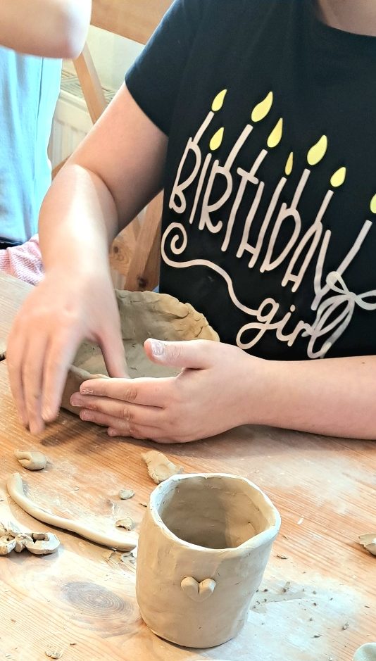 Kinder formen mit Ton Figuren, darunter ein Gesicht mit Hörnern und eine kleine Figur.