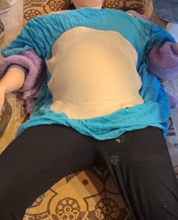 Schwangere Person in blauem Oberteil liegt entspannt auf einer Couch.