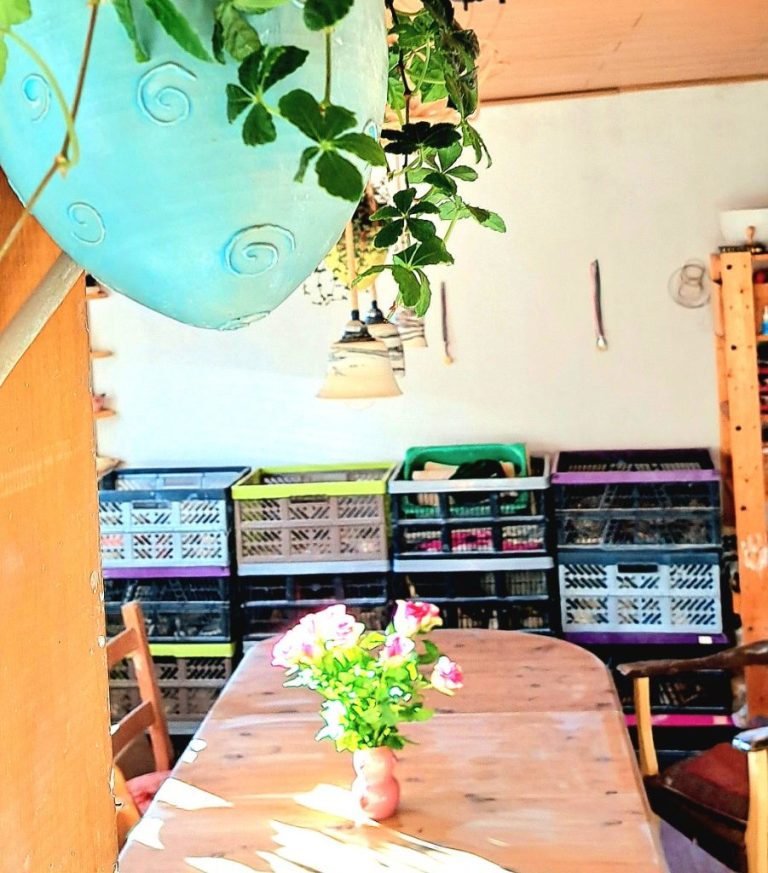 Ein helles Zimmer mit einem Holztisch, Vasen mit Blumen und Regalen im Hintergrund.