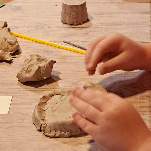 Kinderhände formen mit Knete verschiedene Objekte auf einem Tisch.