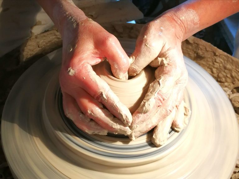 Hände formen eine Tonvase auf einer Töpferscheibe.