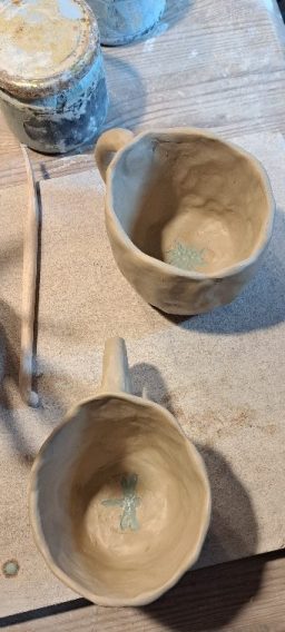 Zwei ungebrannte Tontassen auf einem Tisch, umgeben von Werkzeugen.