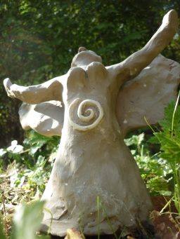 Tonfigur einer tanzenden Frau mit spiralförmigem Muster auf dem Rücken, umgeben von Pflanzen.