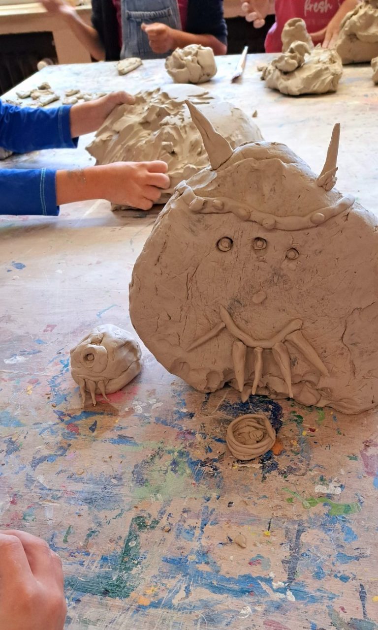 Kinder formen mit Ton Figuren, darunter ein Gesicht mit Hörnern und eine kleine Figur.