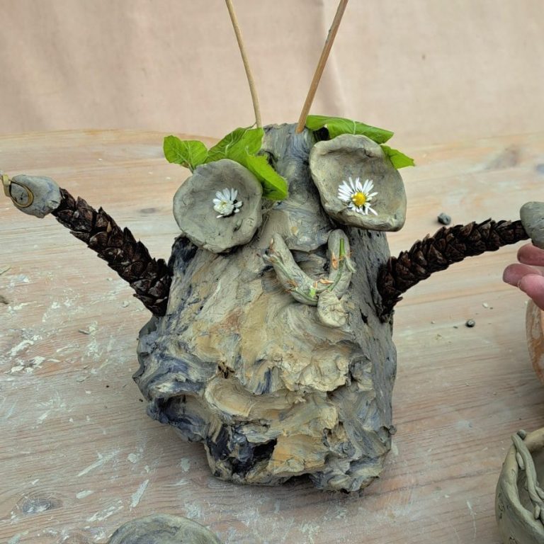Kreatives Gesicht aus Naturmaterialien, mit Zweigen und Blättern als Ohren und Augen.