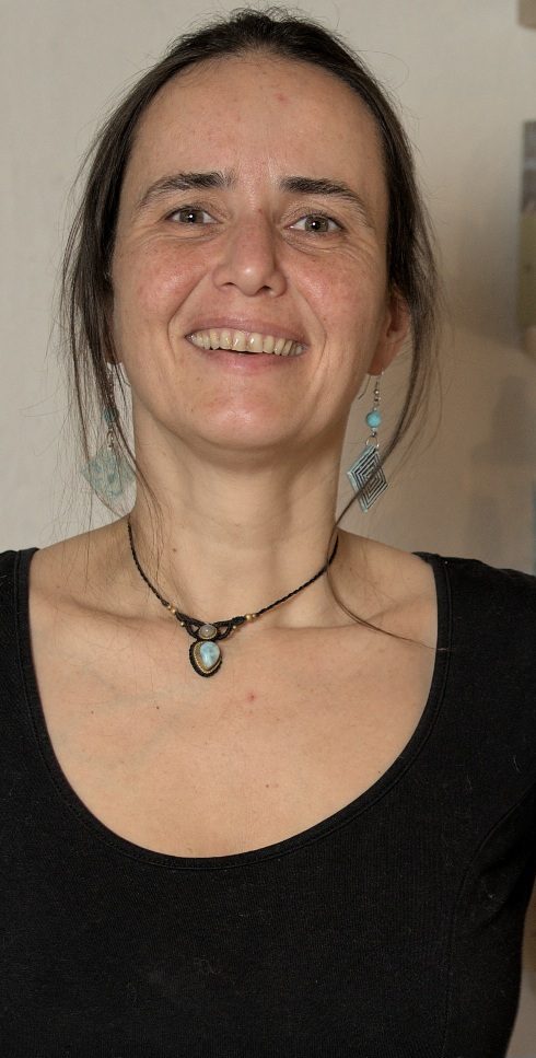 Frau mit langen, dunklen Haaren, schmalem Gesicht und einem schlichten, schwarzen Oberteil.